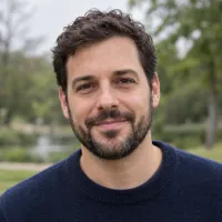 Portrait of a bearded man in a navy sweater in a park.