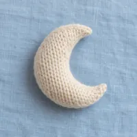 A cream knitted wool moon on pale blue linen.