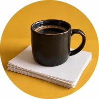 A black cup on a stack of grid paper sheets, on a mustard-yellow background.