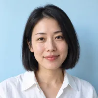 Portrait of a woman with a black bob in a white shirt against a sky-blue wall.