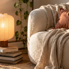 Un coin lecture avec un fauteuil bouclé, un plaid en lin et une lampe en papier