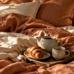 Un lit en lin couleur argile avec un plateau, une théière et un croissant
