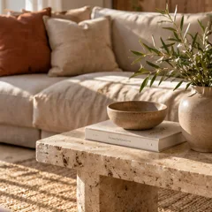 Un salon avec un canapé beige, des coussins terracotta et une table en travertin